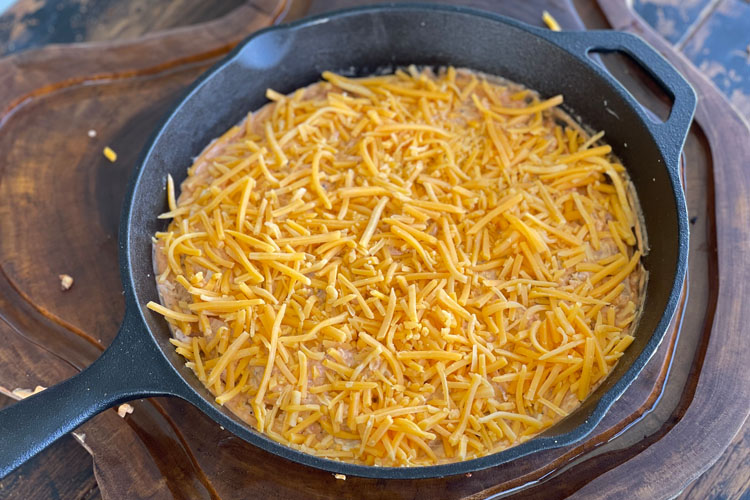 uncooked chicken dip in cast iron skillet with grated cheese on top