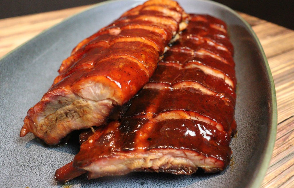 smoked pork ribs slathered in BBQ sauce on a grey plate