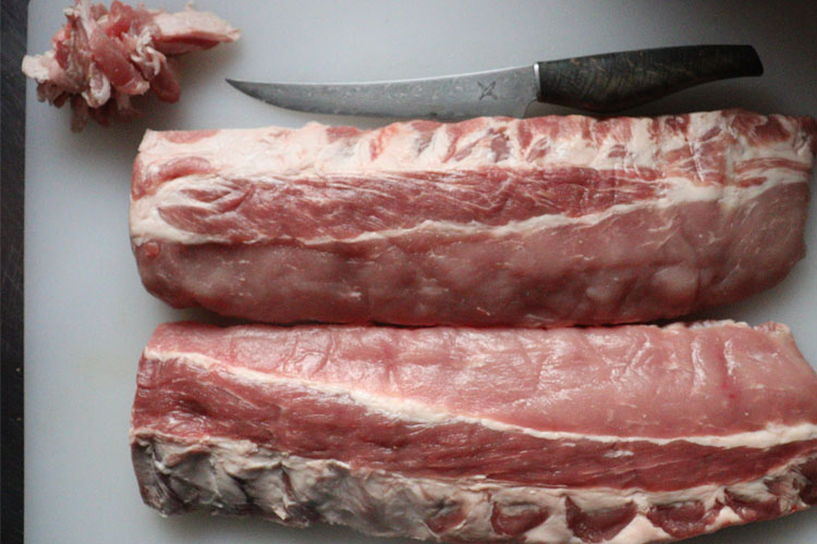 pork ribs on chopping board with knife and trimmed off fat