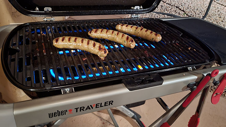 sausages grilling on a weber traveler portable gas grill