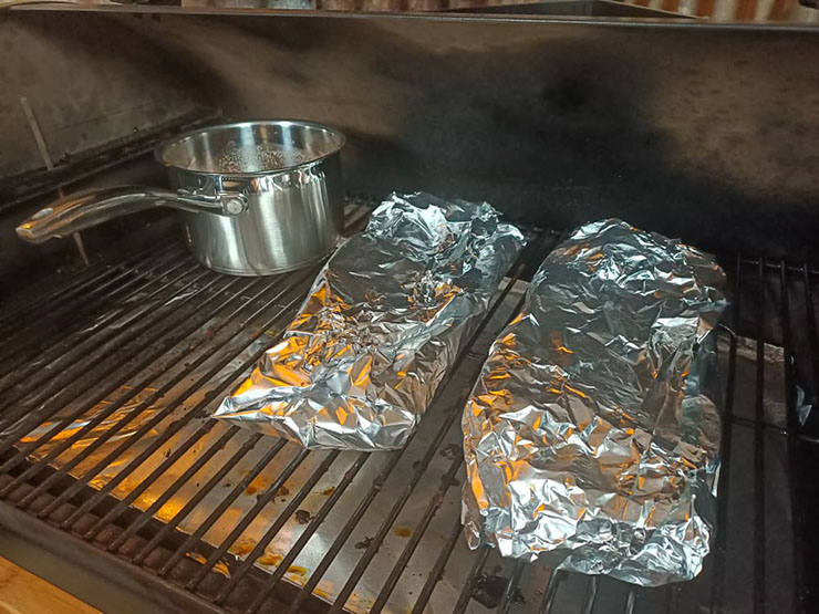 ribs wrapped in foil and a saucepan with bbq sauce on a pellet grill