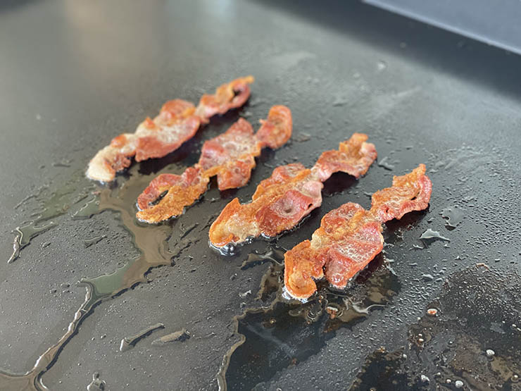 four bacon strips cooking on a griddle