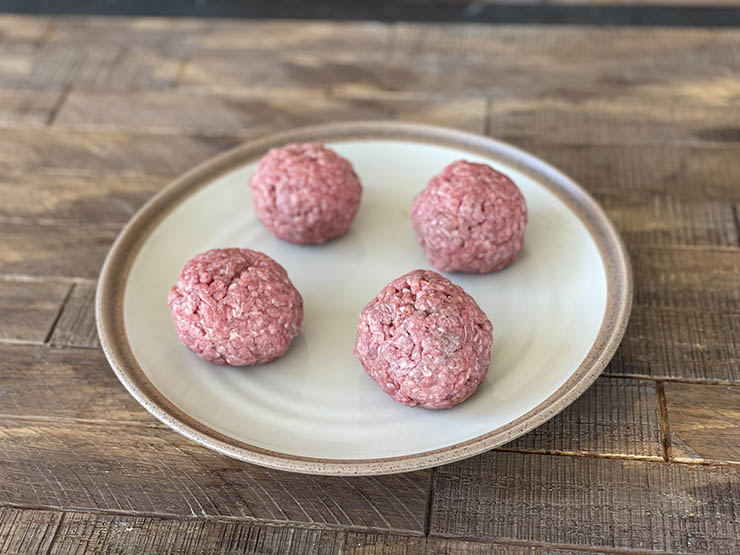 four uncooked beef meat balls on a white plate
