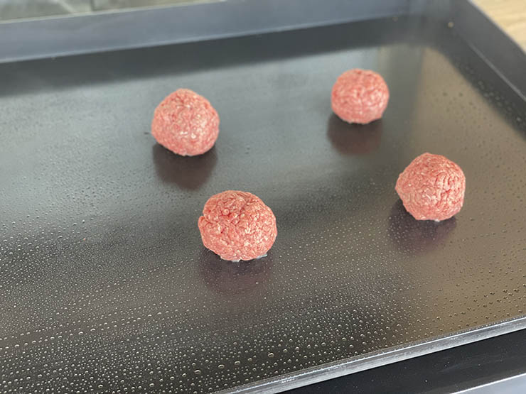four beef meat balls on a griddle