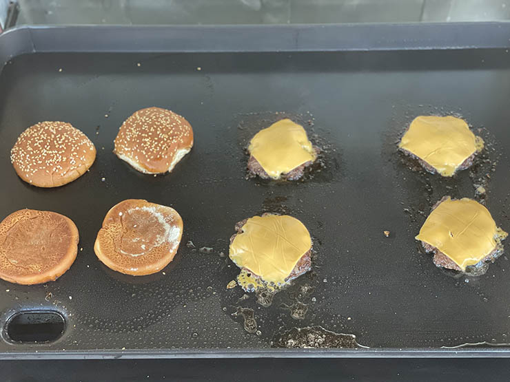 burger buns and beef patties with cheese on a griddle