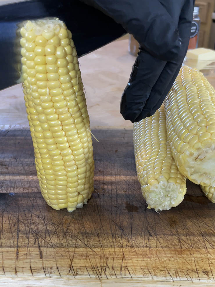 a gloved hand chopping a corn cob with a chef's knife