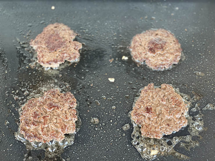 four smashed burger patties on the griddle