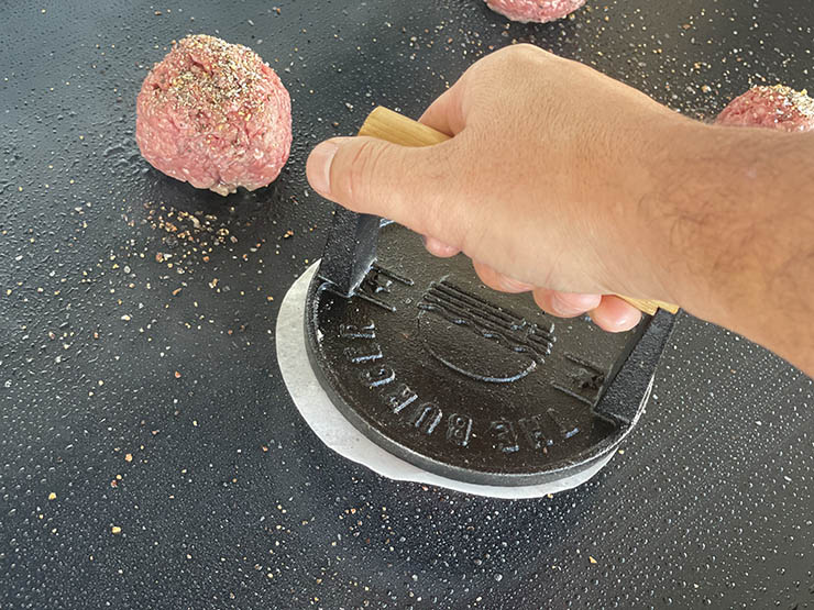 a man smashing beef burger patty on a griddle surface