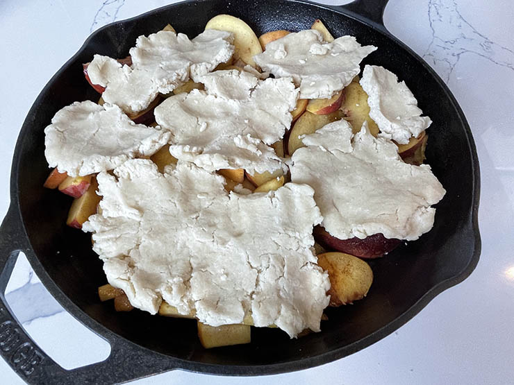 cast iron pan with peach slices topped with uncooked dough