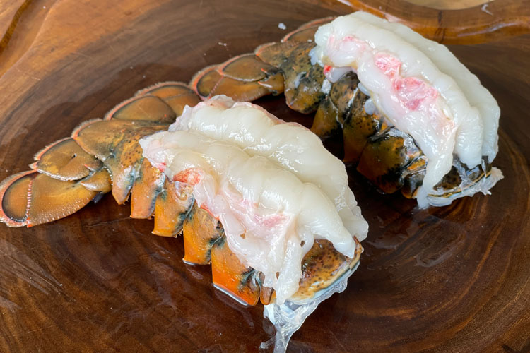 lobster tails with meat sitting on top on a wooden chopping board