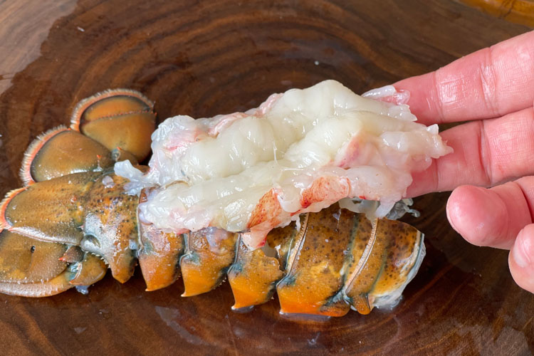 lobster tail on wooden chopping board with hand hold the meat