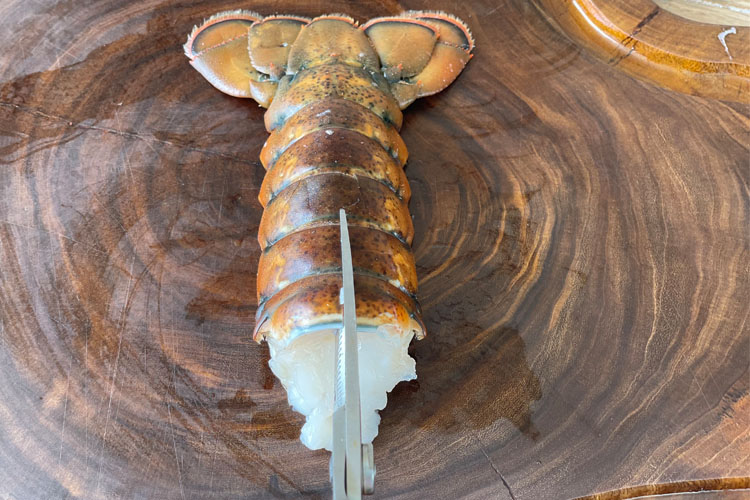 lobster tail on wooden bench with scissors cutting shell