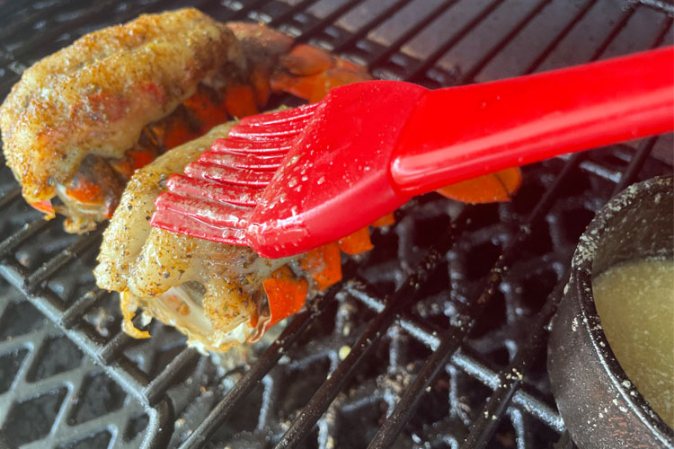 lobster tails on grill being basted with red brush