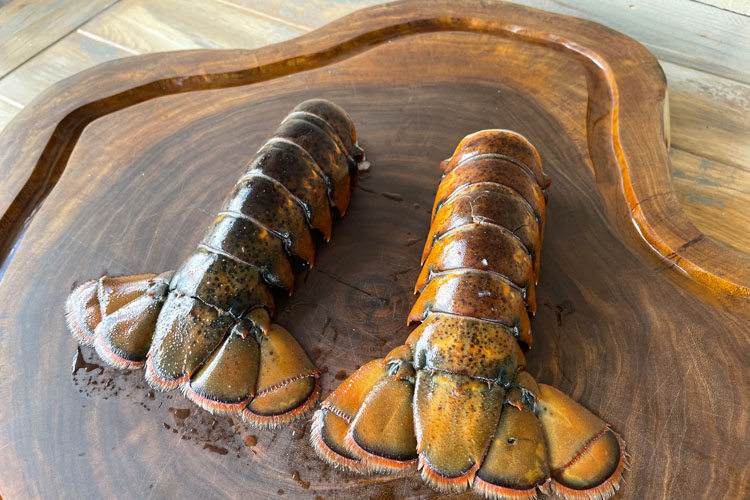2 uncooked lobster tails, back side up on a wooden chopping board