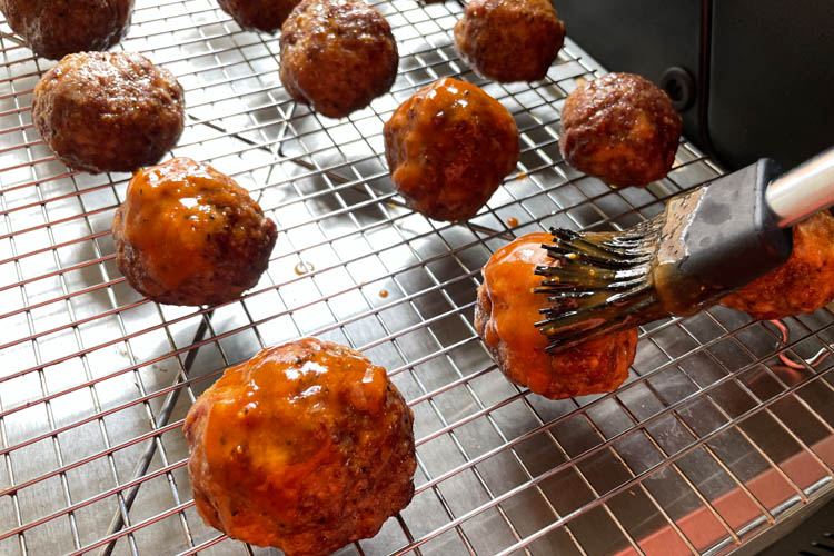 meatballs on a wire rack being brushed with BBQ sauce