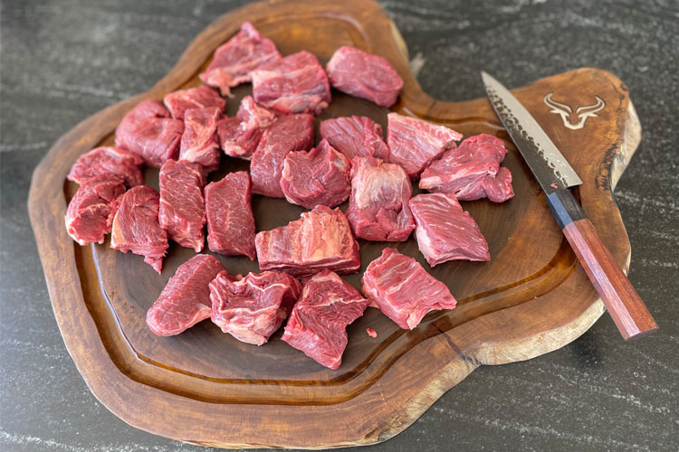 raw cubes of chuck roast on a wooden chopping board
