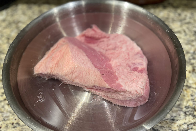 raw piece of corned beef in a sliver bowl