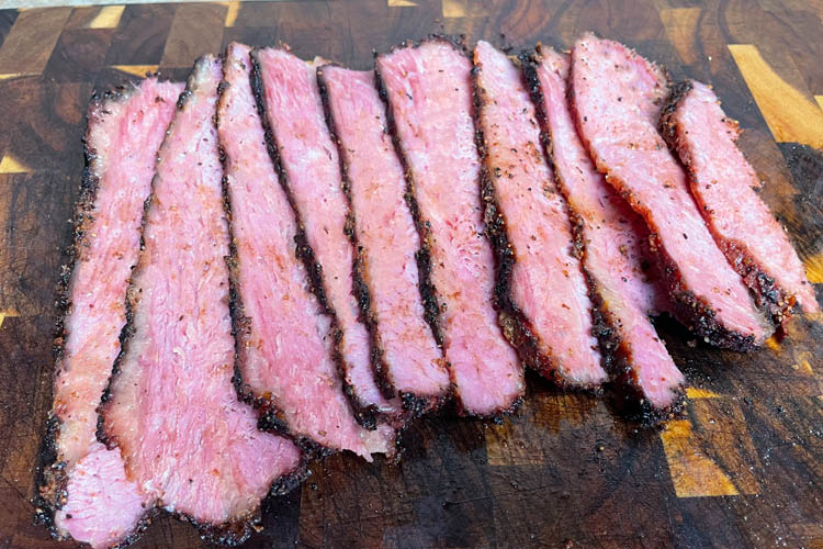 cooked sliced corn beef pastrami on a wooden chopping board