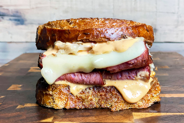 pastrami sandwich with cheese and dressing on a wooden chopping board