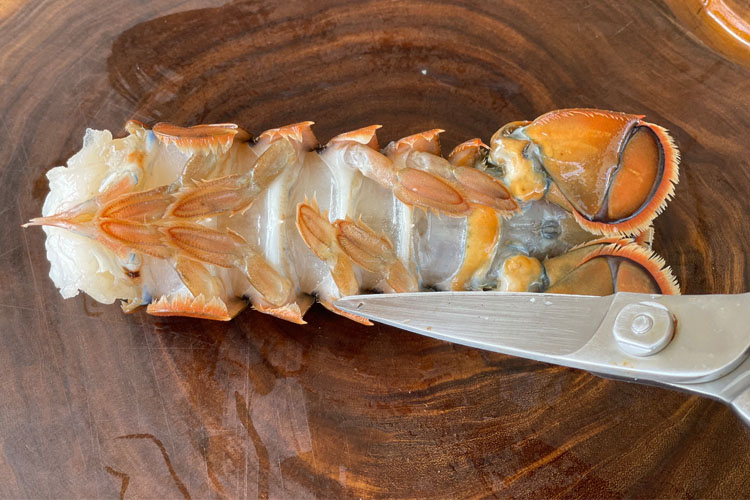 lobster tail underside on wood chopping board with shears