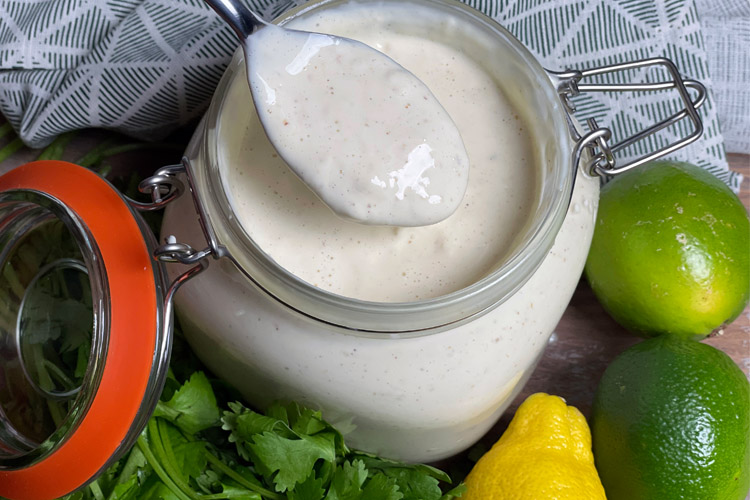 a jar of alabama white sauce with a spoon in it and ingredients around the outside