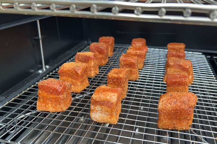 cooked pork belly cubes  on a rack in the smoker