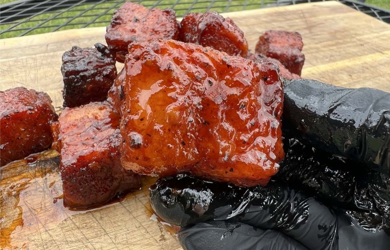 holding pork belly burnt ends in gloved hand