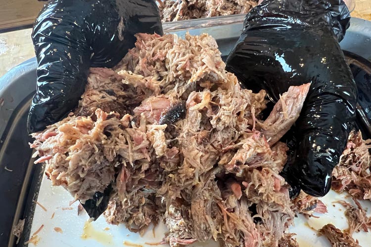 pork butt being shredded with black gloved hands