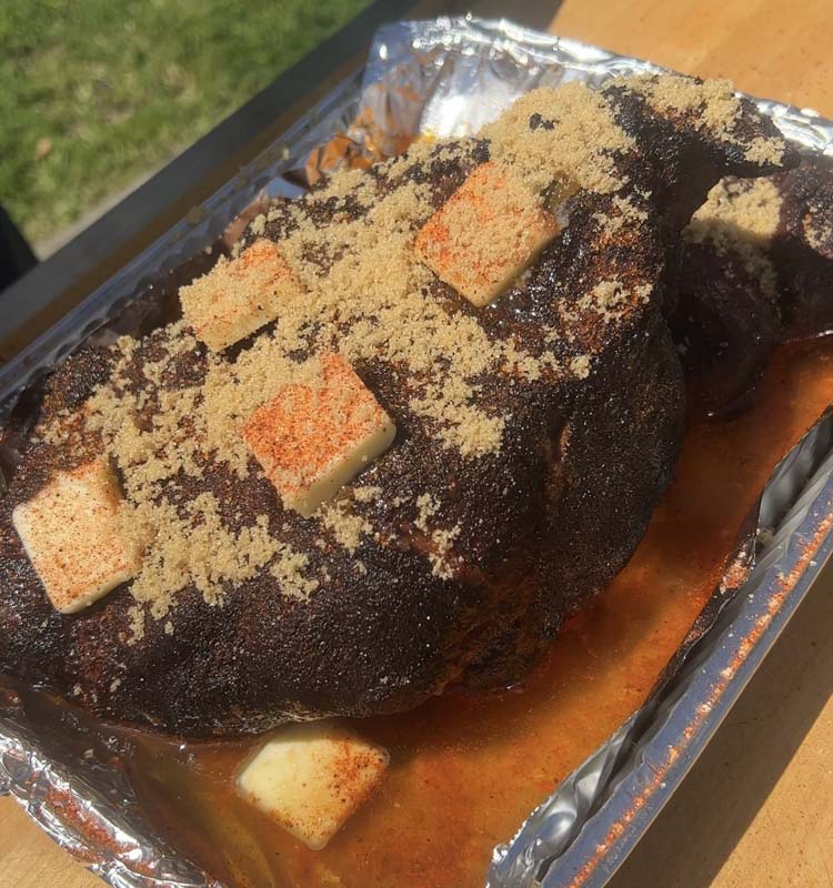 cooked pork butt covered in brown sugar and butter in a foil tray