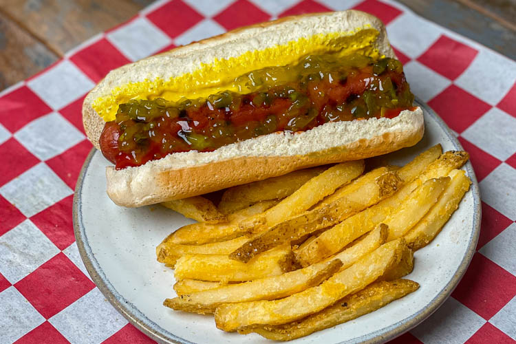 american hotdog and fries on a white plate sitting on a red and white check napkin