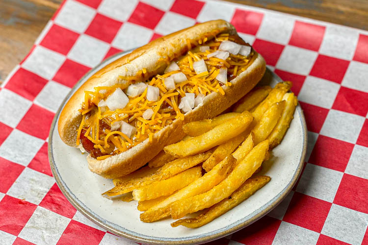 chili cheese dog and fries on a white plate sitting on a red and white check napkin