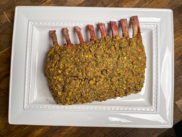 lamb rack covered in pistachio and bread crumb mix on a white plate