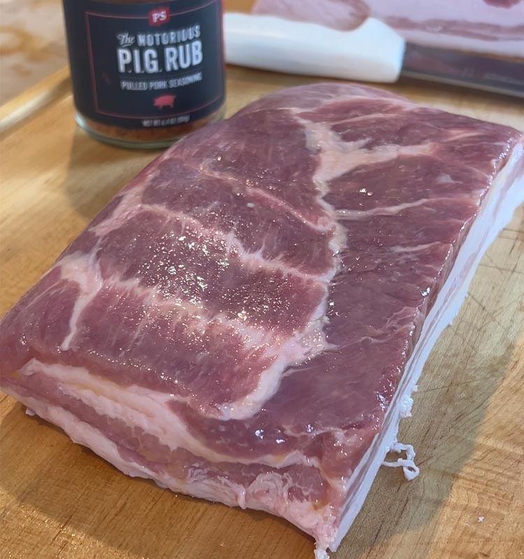 raw pork belly on wooden chopping  board with jar of bbq rub