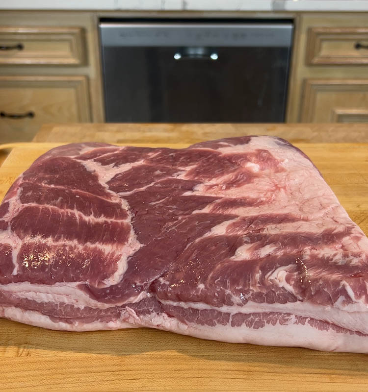 raw slab pork belly on wooden chopping board