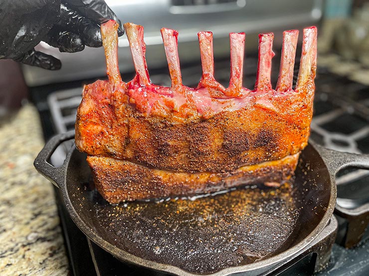 lamb rack seasoned with dry rub searing on a cast iron pan