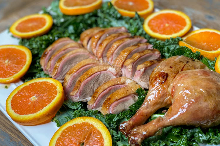 sliced duck on a platter with greens and oranges