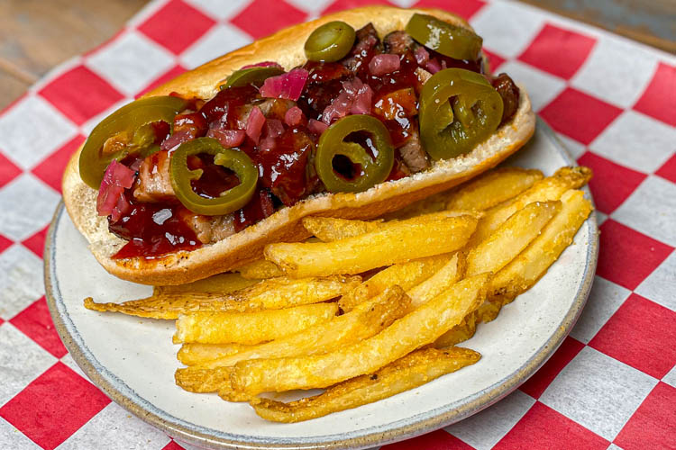 smoked bbq hotdog and fries on a white plate sitting on a red and white check napkin