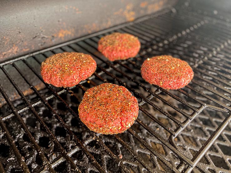 four beef burger patties on a smoker