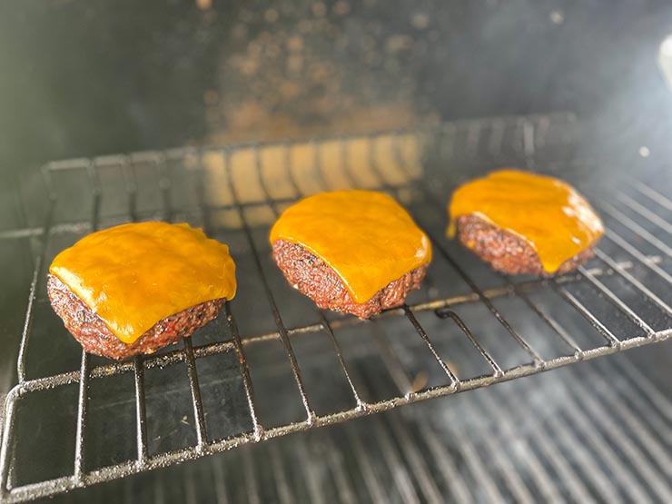 beef burger patties topped with cheddar cheese on the grill grates