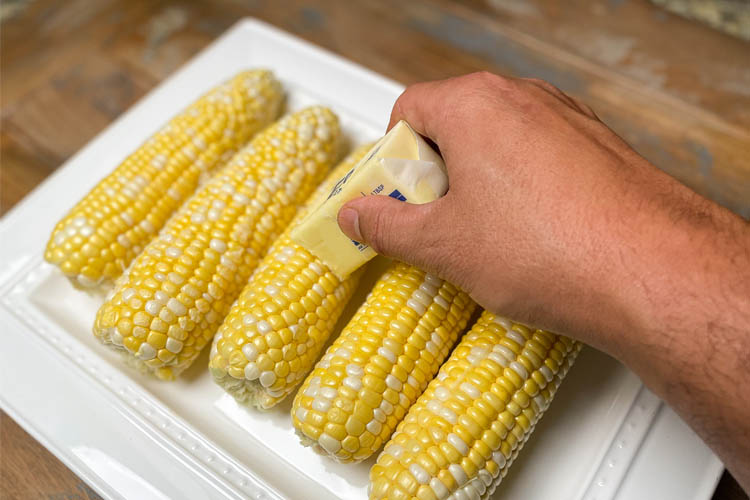 corn on a white plate with hand holding butter