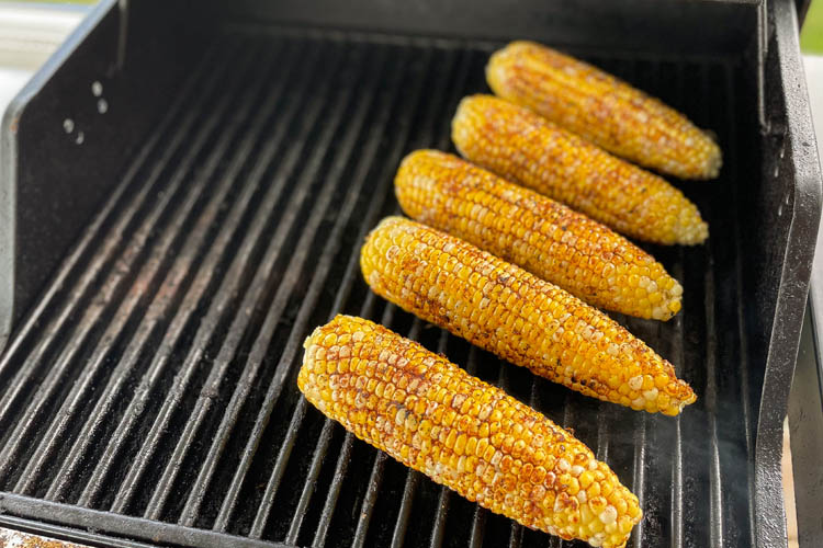 four seasoned corn cobs on a gas grill