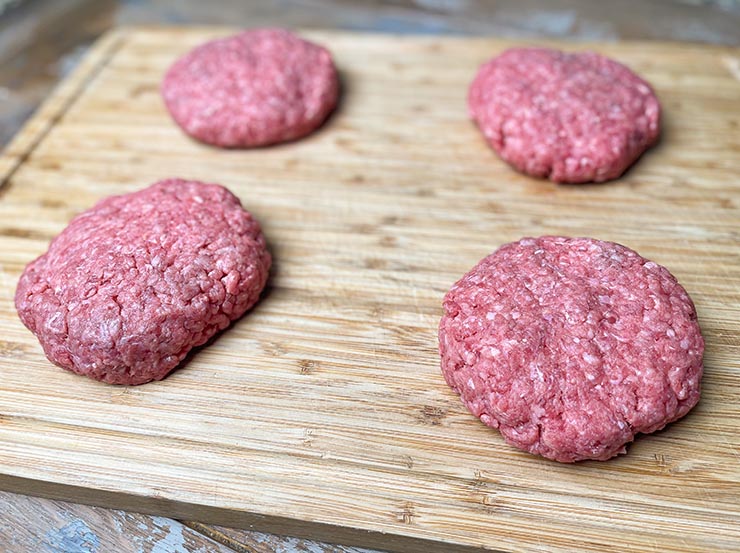 four uncooked beef patties on a wooden board