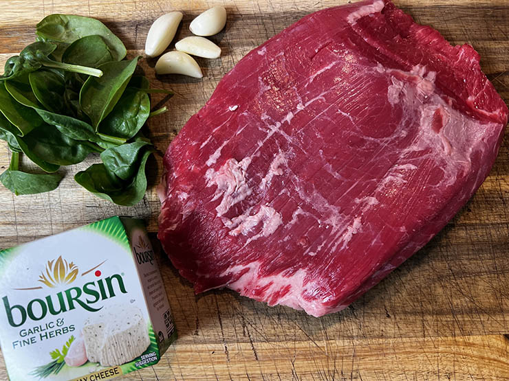 raw flank steak, spinach leaves, garlic cloves and Boursin cheese on a wooden board