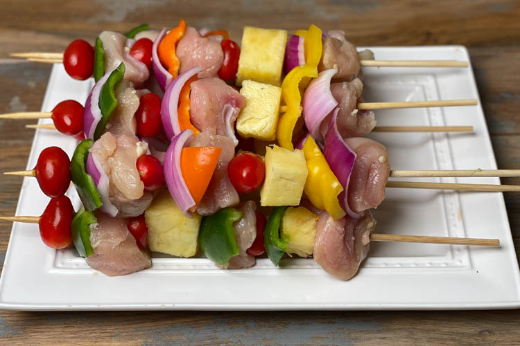 raw chicken kebobs on a white plate