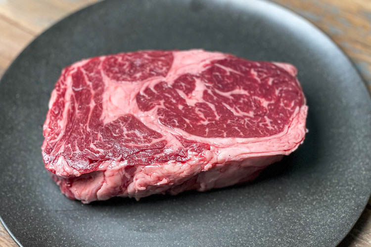 a raw ribeye steak on a black plate