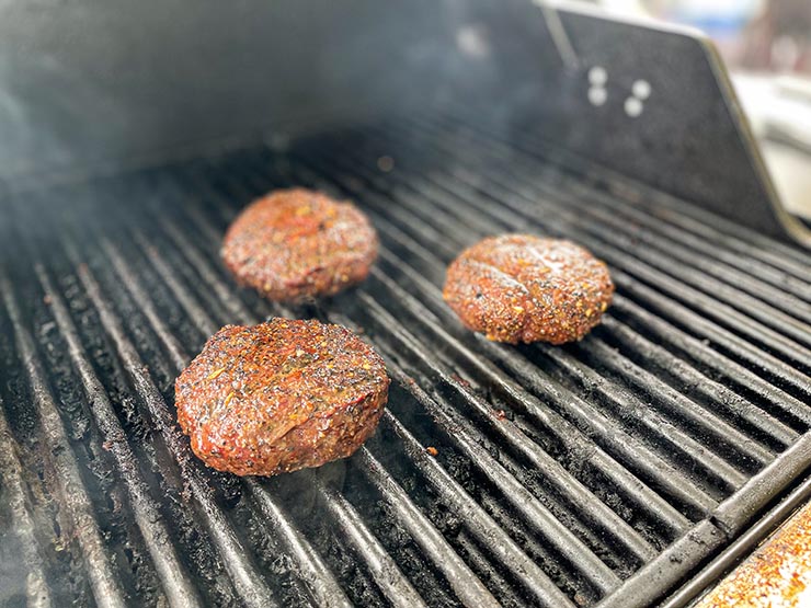 three smoked hamburger patties on a grill