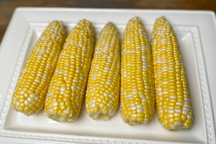four husked corn cobs on a white plate