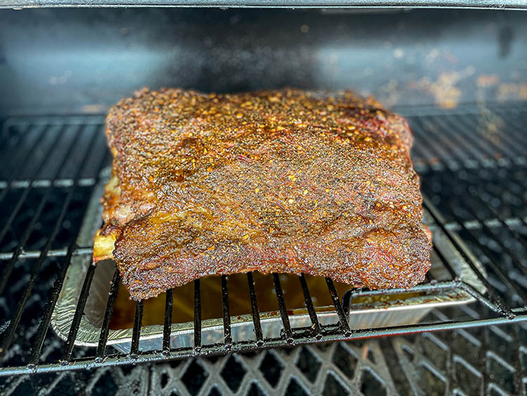 beef ribs on on a smoker rack with the bark not set yet