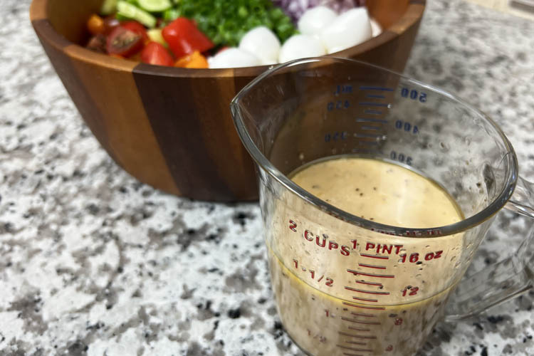 salad ingredients in wooden bowl, dressing ingredients in a glass measuring jug