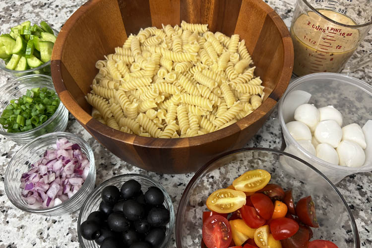 ingredients for pasta salad displayed in separate bowls on marble bench